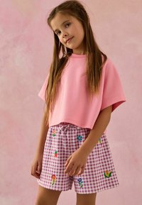 Vaaleanpunainen lyhythihainen crop-top, joka on yhdistetty vaaleanpunaiseen ruutuhameeseen, jossa on värikästä kukka- ja hedelmäkirjontaa.