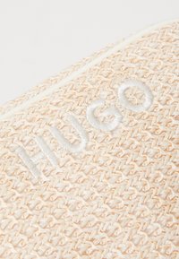 Borsa intrecciata beige con logo "HUGO" cucito in bianco. Presenta un aspetto di fibra naturale testurizzata e un design minimalista.