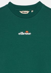 Sötétzöld pulóver, puha anyagból készült, bordázott kerek nyakkivágással és fehér "ellesse" logóval, fölötte színes díszítéssel.