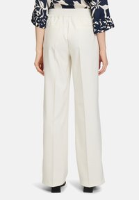 Witte, wijde broek met een gladde textuur en een hoge taille. Beschikt over een elastische tailleband en twee achterzakken.