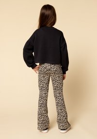 Zwarte cropped sweatshirt met lange mouwen, gecombineerd met flared broek in luipaardprint; heeft een lichtbruine achtergrond en witte sneakers.