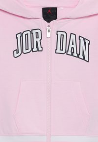 Rozā kapuce ar rāvējslēdzēju, uz kuras ir melns "JORDAN" uzraksts, kangaroo kabata un balta josta. Izgatavota no mīkstas auduma ar gludu tekstūru.