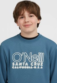 Modrá mikina s okrúhlym výstrihom vyrobená z bavlnenej zmesi, s bielym vyšívaným textom: „O’Neill SANTA CRUZ CALIFORNIA U.S.A.“