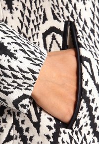 Svartvitt mönstrat textil med en synlig ficka. Hand in i fickan, vilket visar tygstrukturen och kantdetaljen.