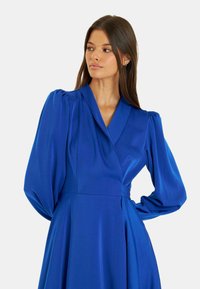 Königsblaues Kleid mit Wickeldesign, langen voluminösen Ärmeln und taillierter Taille, mit einer weichen, glatten Textur.