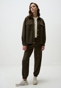 Completo in morbido tessuto marrone con camicia a bottoni e pantaloni della tuta abbinati. Le sneakers presentano dettagli bianchi e beige. Design semplice e rilassato.