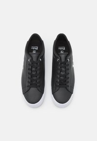 Černé kožené tenisky s hladkým povrchem, bílé gumové podrážky a černé tkaničky. Obsahují logo na jazyku a elegantní, minimalistický design.