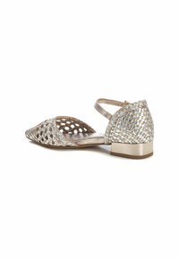 Zapatos planos y abiertos en la punta con un upper tejido en un dorado metálico, correa ajustable en el tobillo y un tacón bajo y minimalista. Superficie texturizada con un diseño de malla.
