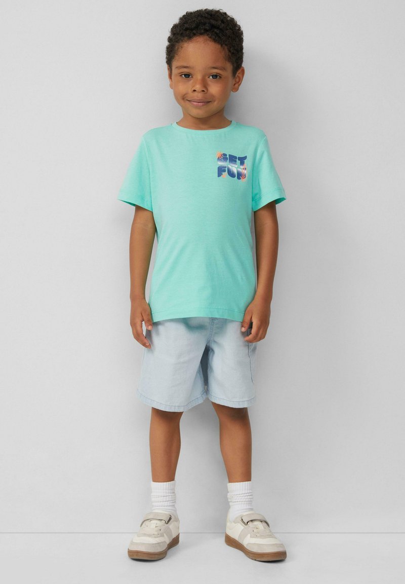 Turquoise T-shirt met korte mouwen met "GET FUN" grafiek, gecombineerd met lichtblauwe shorts en witte sokken, gedragen met crèmekleurige sneakers.