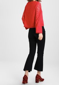 Czerwony koronkowy krótki top z szerokimi rękawami, zestawiony z czarnymi dzwonowymi jeansami i czerwonymi butami na słupku w cętki.