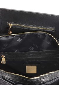 Juodos tekstūruotos odos krepšio vidus su užtrauktuku kišenėje, auksiniu užtrauktuku ir logotipo žyma. Išklotas juoda medžiaga su subtiliu prekės ženklo raštu.