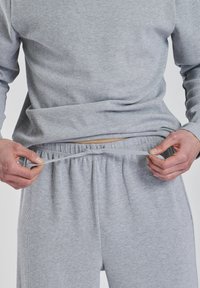 Grå, ribbet langærmet skjorte og matchende bukser med elastisk talje. Modellen justerer snoretrækket på bukserne.