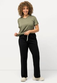 Olijfgroen V-hals t-shirt gecombineerd met zwarte joggingsbroek met zijzakken. Model draagt lichtgekleurde schoenen.