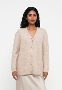 Cardigan tricotat bej, fabricat dintr-un material moale și pufos. Design cu decolteu în V, dotat cu o linie de șase butoane rotunde, având mâneci lungi și o croială lejeră.
