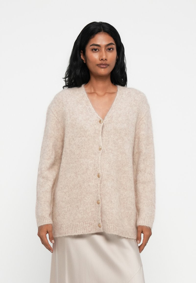 Cardigan tricotat bej, fabricat dintr-un material moale și pufos. Design cu decolteu în V, dotat cu o linie de șase butoane rotunde, având mâneci lungi și o croială lejeră.