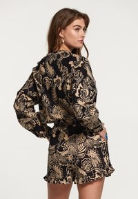 Outfit floreale nero e beige con tessuto testurizzato. Presenta un orlo arricciato, maniche lunghe e una vestibilità rilassata.