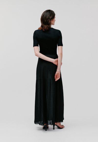 Schwarzes Maxikleid mit figurbetontem Oberteil und plissiertem Rock, kurzen Ärmeln und glatter Textur. Tragen mit schwarzen High Heels, Rückansicht.