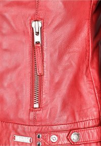 Rød læderjakke med en sølvlynlås, tekstureret finish og metalsnaps med mærket "MUSTANG." Tydelige sømme og detaljer er synlige.