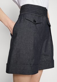 Donkere denim shorts met een hoge, geplooide tailleband, zijzakken en opgerolde boorden. Voorzien van een enkele knoopsluiting op de achterzak.