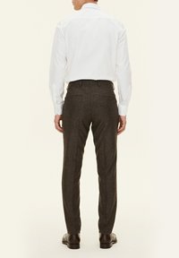 Camicia bianca a maniche lunghe con polsini a bottoni, abbinata a pantaloni grey su misura con una texture liscia e due tasche posteriori.