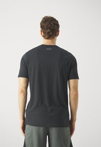 T-shirt nera a maniche corte in cotone. Presenta un logo circolare sul colletto posteriore. Abbinata a pantaloni corti grigi.