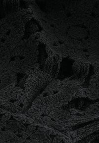 Czarna dzianina z fakturowanym, ażurowym wzorem z motywami kwiatowymi i wypukłymi akcentami. Miękka i lekko aksamitna w dotyku.