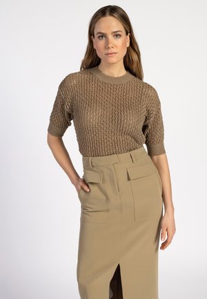 Bruine gebreide trui met korte mouwen en een losse structuur, gecombineerd met een hoog-waist beige kokerrok met twee voorzakken en een split.