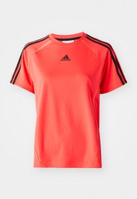 Trumpas, ryškiai koralų spalvos sportinis marškinėlis su trumpomis rankovėmis, pagamintas iš lengvos medžiagos. Yra juodas Adidas logotipas ir trys juodos juostelės ant kiekvieno peties.