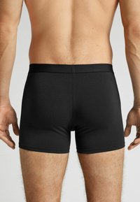 Svarta boxershorts med en slät textur, som har ett mjukt midjeband och en åtsittande passform, utformade för komfort och stöd.