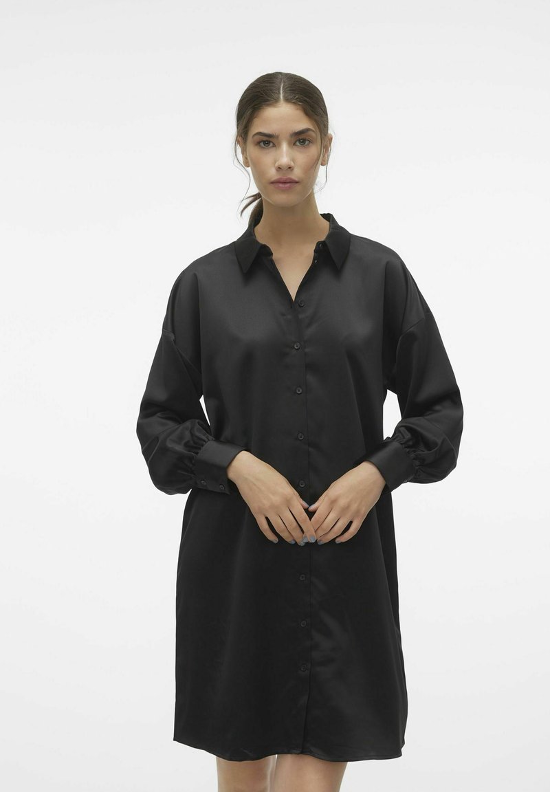Abito camicia nero con apertura a bottoni, maniche lunghe e colletto. Realizzato in tessuto liscio e lucido; vestibilità comoda con polsini arricciati.