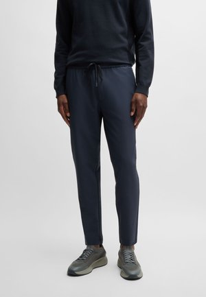 Navy jogger-housut, joissa on elastinen vyötärö ja nauha. Sileä pinta, kapeneva muotoilu, yhdistettynä harmaisiin lenkkikenkiin.