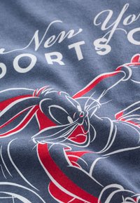 Lapin de dessin animé tenant une corde rouge et blanche sur un tissu bleu avec un texte partiellement visible "New York Sports."