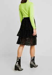 Haut ajusté à manches longues vert vif, jupe noire en dentelle à volants, et bottes à talons métalliques avec un motif en zigzag. Texturé et superposé.