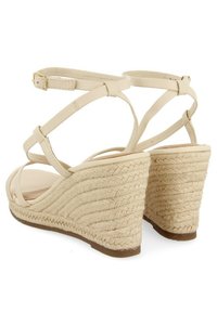 Beige wedge-sandaalit, joissa on punottu juuttipohja, ristiin menevät hihnat ja nilkkahihna soljella. Karkea pohja.