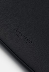Surface en cuir noir texturé avec le nom de la marque « Seidenfelt Manufaktur » embossé au centre.