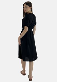 Abito nero al ginocchio con maniche corte, vita cintrata e vestibilità ampia. Realizzato in tessuto leggero, presenta un design semplice ed elegante.