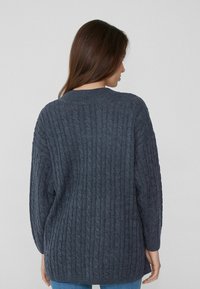 Dunkelgrauer Kabelstrickpullover mit langen Ärmeln. Hat eine gerippte Textur und einen Rundhalsausschnitt. Lockerer Schnitt mit seitlichen Schlitzen am Saum.