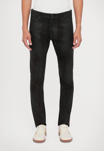 Schwarze Jeans aus Denim im Slim-Fit, mit einer dezenten gebürsteten Textur. Vordertaschen und Knopfverschluss, kombiniert mit weißen Sneakern.