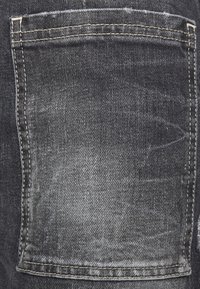 Tejido de denim negro con un bolsillo trasero con costuras visibles y una textura deslavada. La superficie muestra sutiles variaciones de color y desgaste.