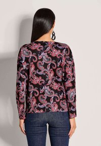 Langärmlige Bluse aus schwarzem Stoff mit einem bunten Paisleymuster in Rot, Blau und Weiß. Gerader Saum und lockere Passform.