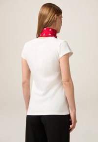 Witte T-shirt met korte mouwen en een ronde hals; voorzien van een rode bandana-stijl nek sjaal met witte patronen. Glad katoenen stof.