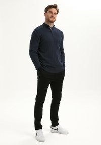 Marineblauwe geribbelde pullover met een ritskraag, zwarte slim-fit broek en witte sneakers met zwarte accenten. Eenvoudig en modern ontwerp.