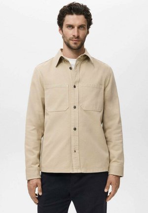 Beige cotton shirt jacket with long sleeves, front pockets, button closure, and a structured collar. Smooth texture and relaxed fit.