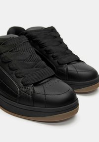 Sneakers neri in pelle con una finitura liscia, caratterizzati da spesse stringhe nere, un design perforato sulla punta e una suola in gomma testurizzata.