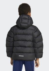 Giacca a vento nera con cappuccio, caratterizzata da sezioni trapuntate per l'isolamento, texture liscia e un accento riflettente vicino al fondo.