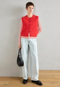 Κόκκινο ριγωτό πλεκτό γιλέκο με μαύρα κουμπιά πάνω από λευκή και κόκκινη ριγέ μπλούζα, συνδυασμένο με ανοιχτό μπλε παντελόνι με φαρδιά πόδια και μαύρες loafers. Μαύρη τσάντα.