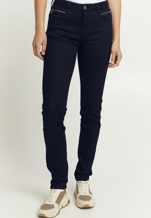 Slim-Fit schwarze Jeans mit Reißverschlusstaschen vorne. Bietet eine glatte Textur und einen leichten Stretch, kombiniert mit hellen Sneakers.