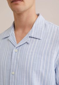 Chemise à manches courtes bleu clair avec des rayures blanches verticales, un col à revers et deux boutons, fabriquée dans un tissu texturé.