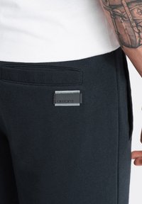 Jogging en coton noir avec une texture lisse, dotés d'une fausse poche cousue et d'une patch logo rectangulaire à l'arrière.