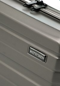 Valigia rigida grigia con superficie texturizzata, zip nere e una placca d'argento con la scritta "Wittchen" in rilievo.